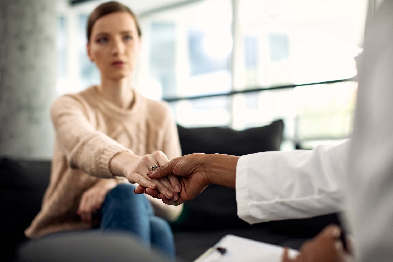 Close-up of female patient and mental health professional holdin Close-up of woman and her psychotherapist holding hands during appointment at the clinic.
